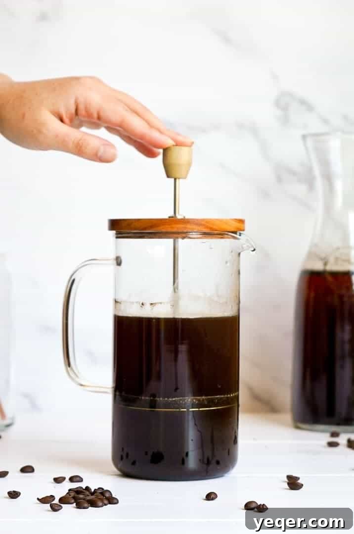 Smooth Cold Brew Overnight Delight 5 A hand pressing a French press plunger down to filter the cold brew coffee, demonstrating the final step of preparation.