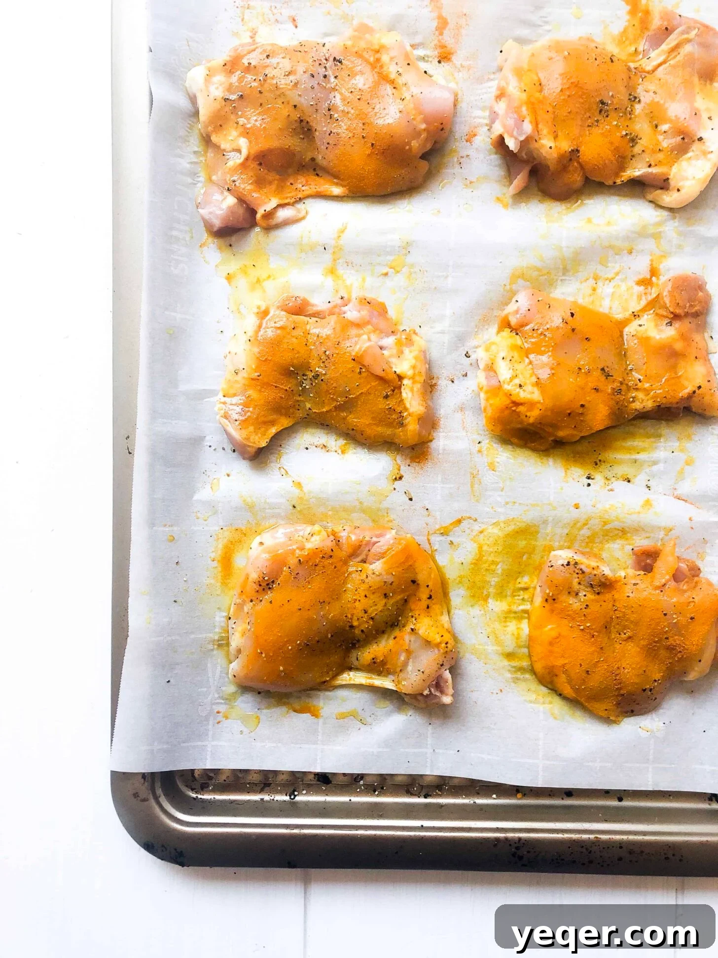 A sheet pan with six chicken thighs coated with turmeric and black pepper