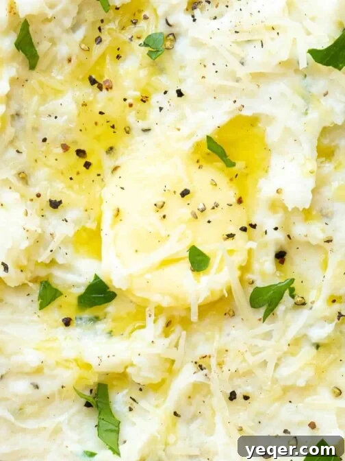 A close up of a bowl of mashed potatoes with parmesan, butter, herbs, and pepper.