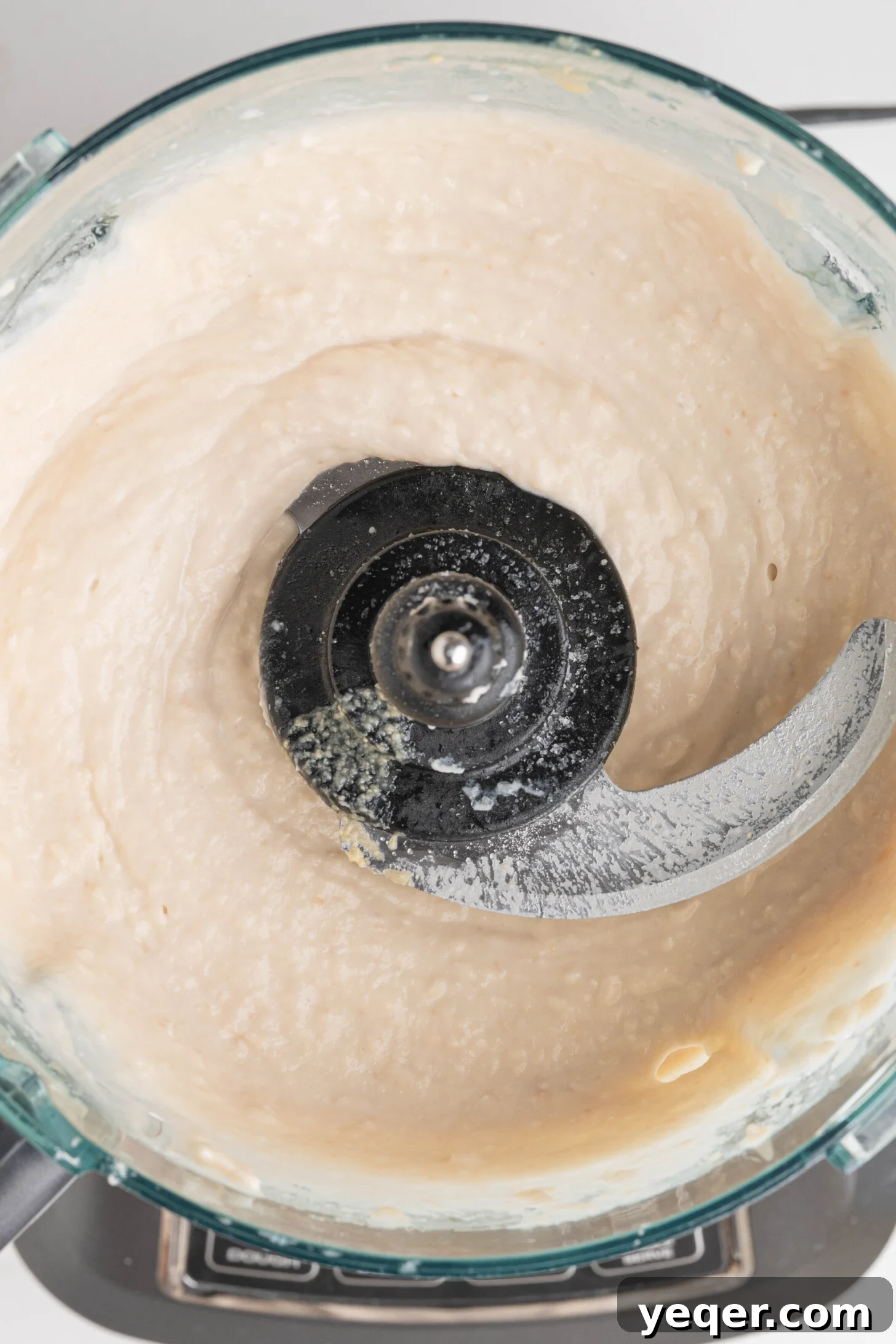 Close-up of creamy white bean hummus swirling in a food processor.