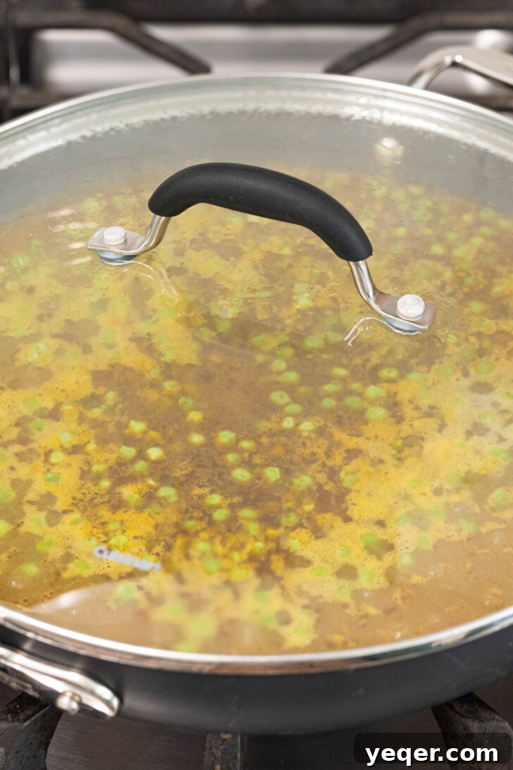 Vibrant Puerto Rican Arroz con Camarones 5 A pot with rice, broth, and peas brought to a boil and then covered to simmer.