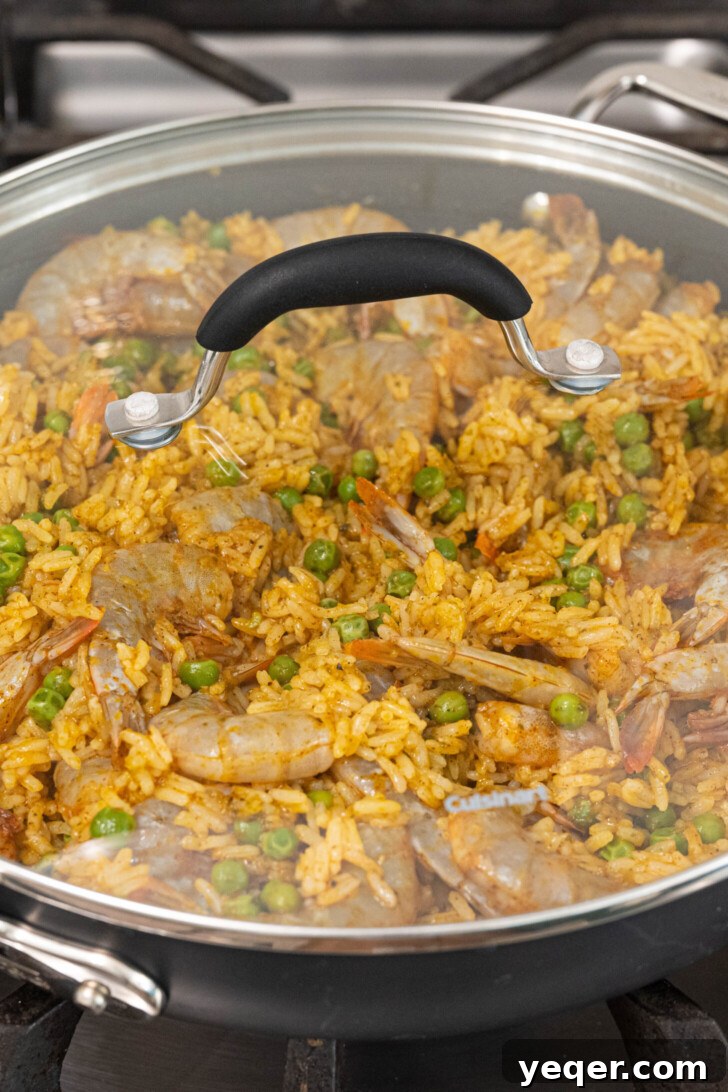 Vibrant Puerto Rican Arroz con Camarones 7 Seasoned shrimp being gently folded into a pan of cooked rice.