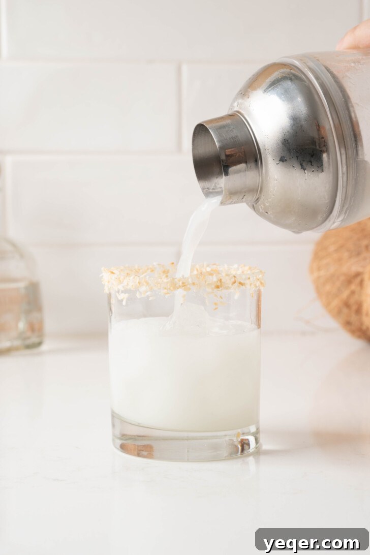 Effortless Silky Coconut Margarita 7 A coconut margarita being double-strained from a shaker into a prepped glass over fresh ice.