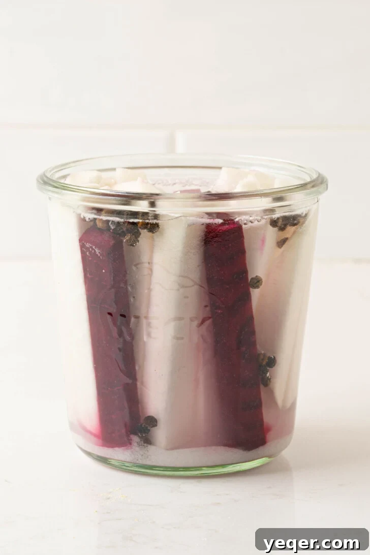 Easy 5-Ingredient Pink Pickled Turnips 6 Sliced turnips and beets being placed into a sterilized jar with pickling spices and vinegar.