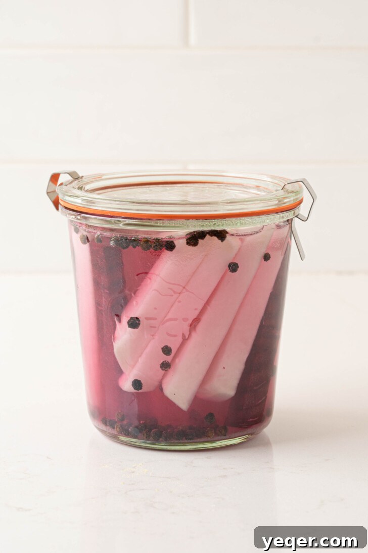 Easy 5-Ingredient Pink Pickled Turnips 7 A hand shaking a sealed jar containing turnips, beets, and pickling liquid.
