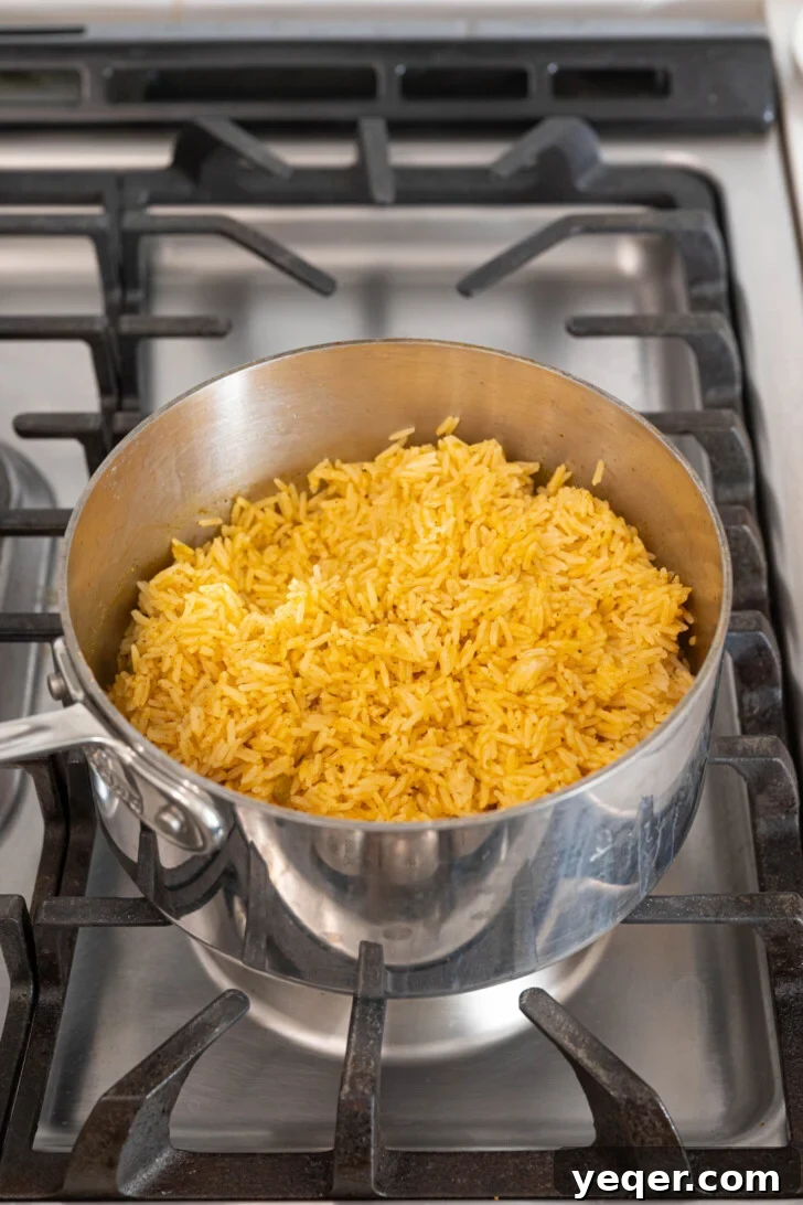Fluffy 30-Minute Yellow Rice 8 Fluffy yellow rice in a pot, being gently stirred with a spoon.