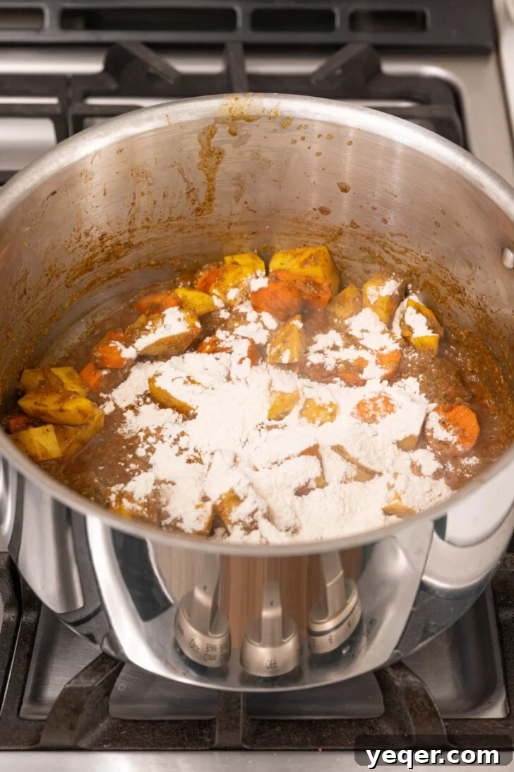 Carne Guisada The Ultimate Beef Stew 8 Flour over potatoes and carrots in a pot.