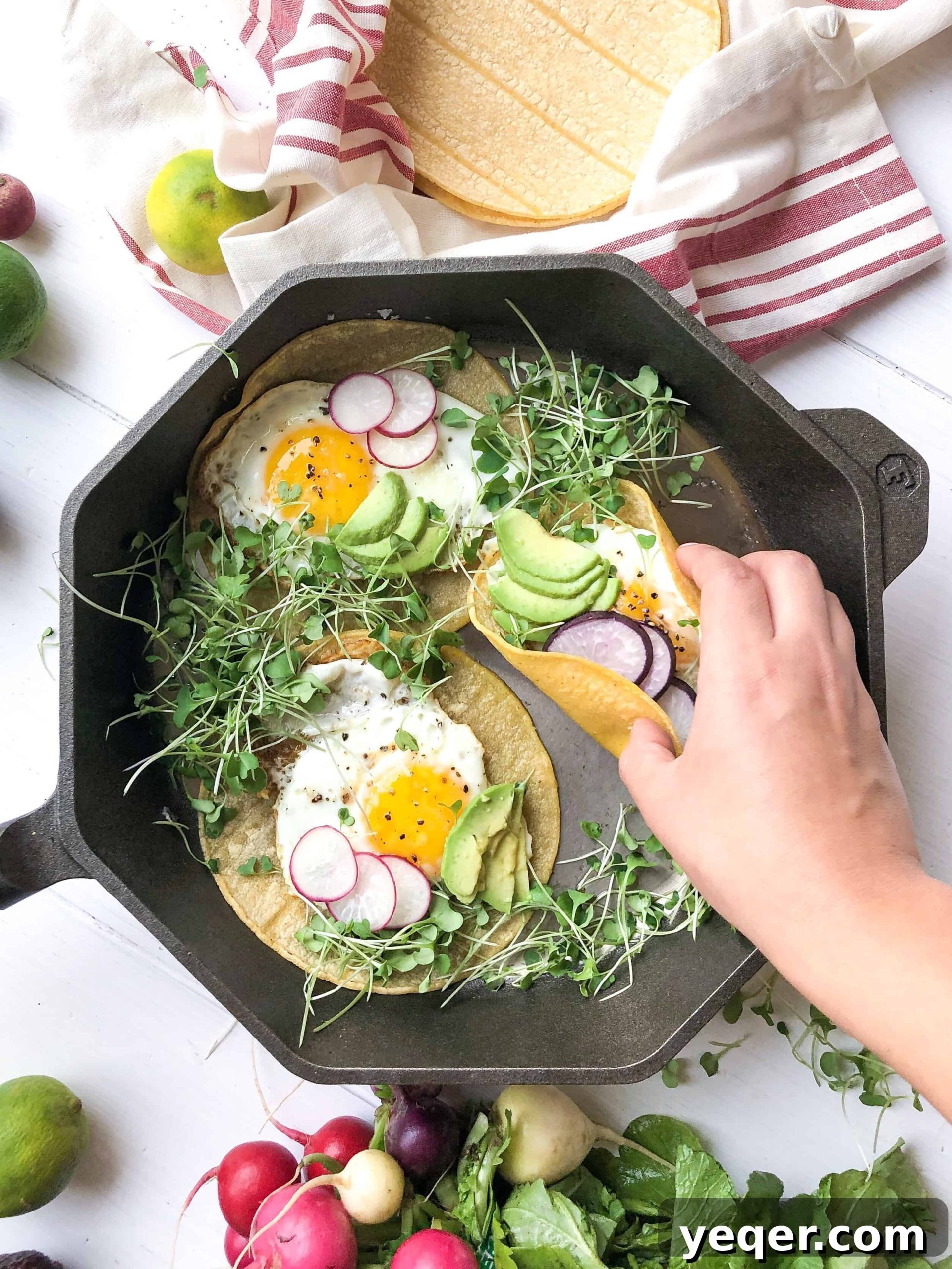 Sunrise Veggie Tacos 4 A close-up view of three perfectly prepared vegetarian breakfast tacos with a hand reaching for one, showcasing the vibrant fillings and runny egg yolk.