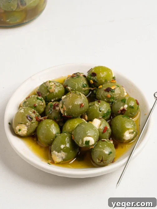 Exquisite Marinated Olives 8 Close-up of elegantly stuffed marinated olives arranged on a white serving plate, garnished with fresh herbs, truly ready to be savored.