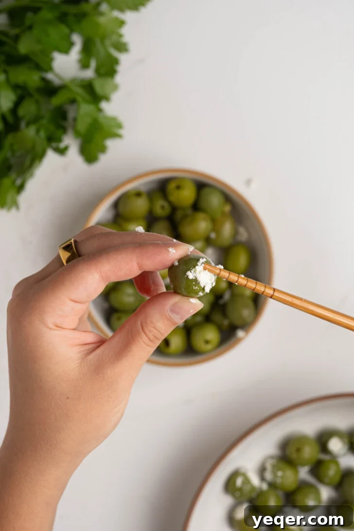 Exquisite Marinated Olives 4 A hand gently stuffing a plump green olive with a small, creamy piece of feta cheese.