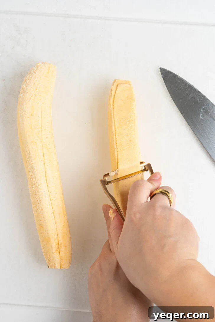 Crispy Plantain Delights 6 A peeled green plantain being sliced thinly with a vegetable peeler.