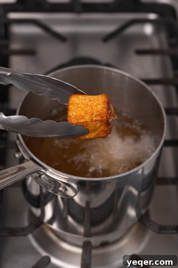 Crispy Queso Frito with Tropical Guava Drizzle 7 Golden brown, crispy fried cheese cubes being carefully removed from hot oil in a deep fryer.