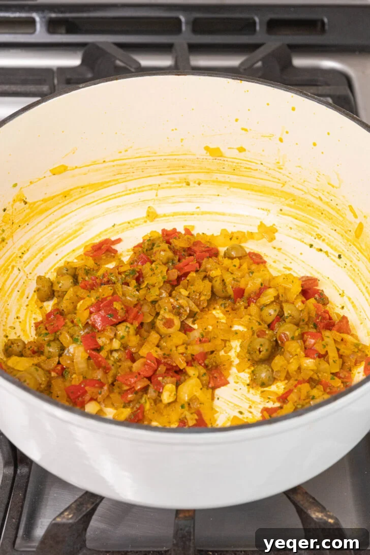 Vibrant Puerto Rican Seafood Rice 5 A pot on a stovetop filled with sautéing onions, peppers, olives, and spices.