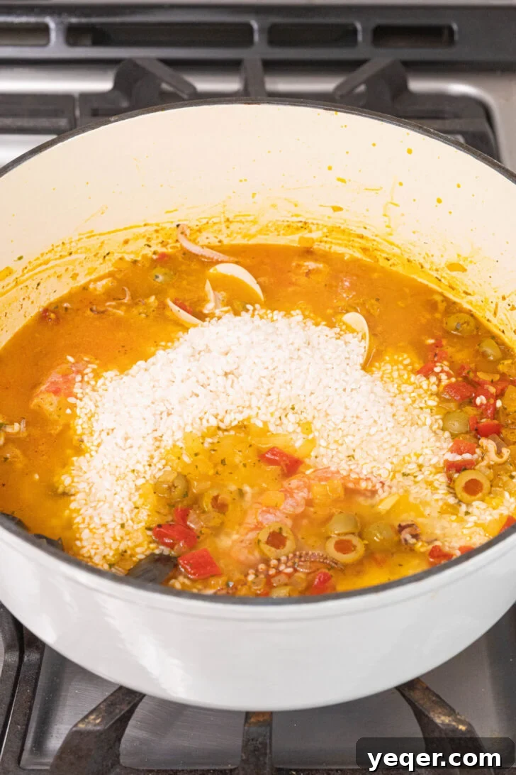 Vibrant Puerto Rican Seafood Rice 7 Rice and water being stirred into the pot with seafood and vegetables.