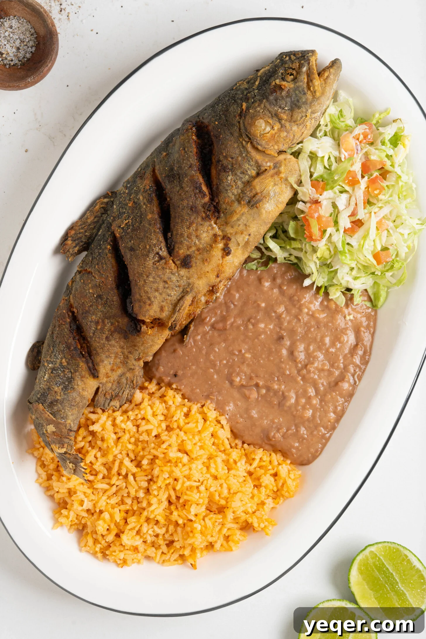 Crispy Whole Fried Mojarra 2 A vibrant platter featuring golden-brown Mojarra Frita, fluffy white rice, savory black beans, and a fresh green salad, perfectly arranged for a delicious meal.