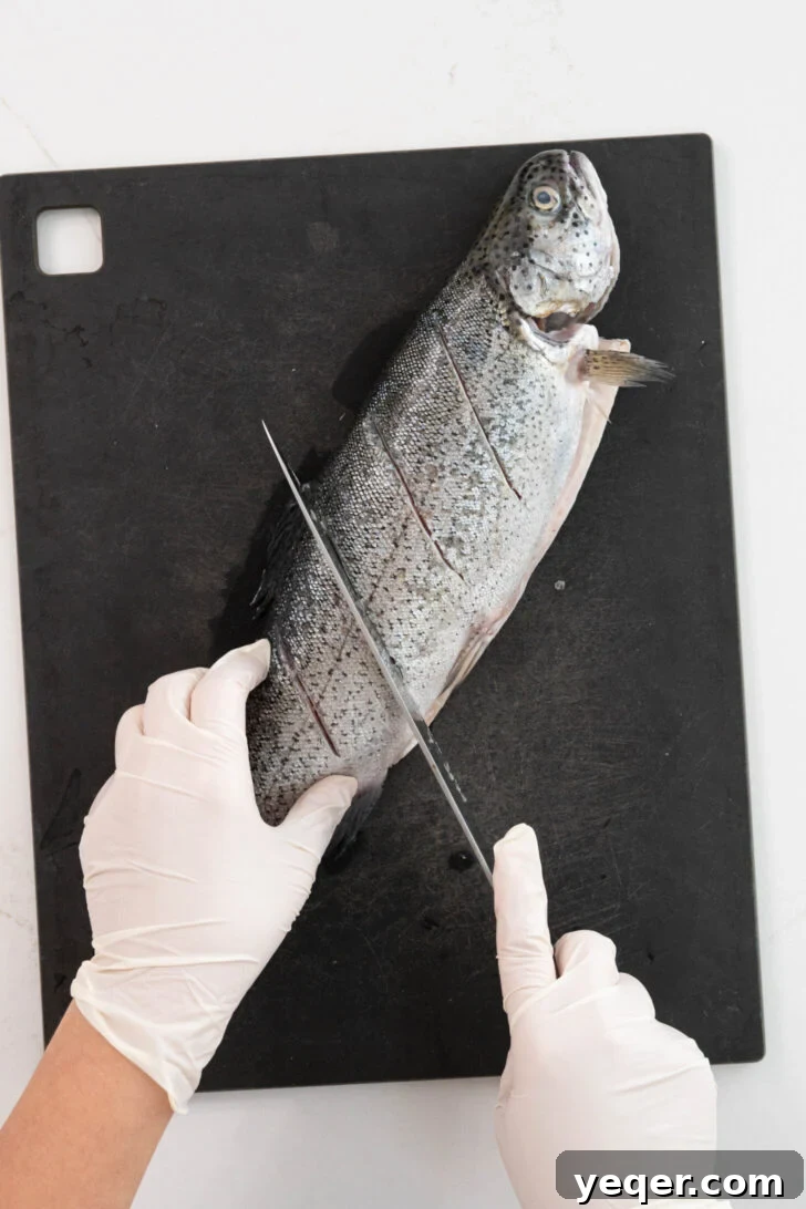 Crispy Whole Fried Mojarra 4 A whole fish receiving small, precise cuts into its flesh, preparing it for optimal seasoning and even cooking.