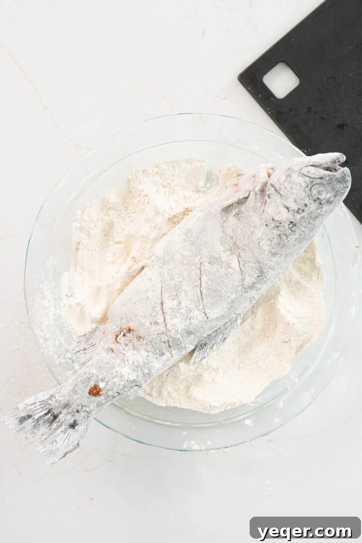 Crispy Whole Fried Mojarra 6 A whole fish being evenly coated in flour on a plate, preparing it for a crispy fry.
