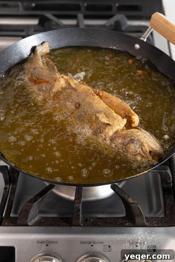 Crispy Whole Fried Mojarra 7 A whole fish sizzling as it fries in a deep pot of hot oil, becoming golden and crispy.