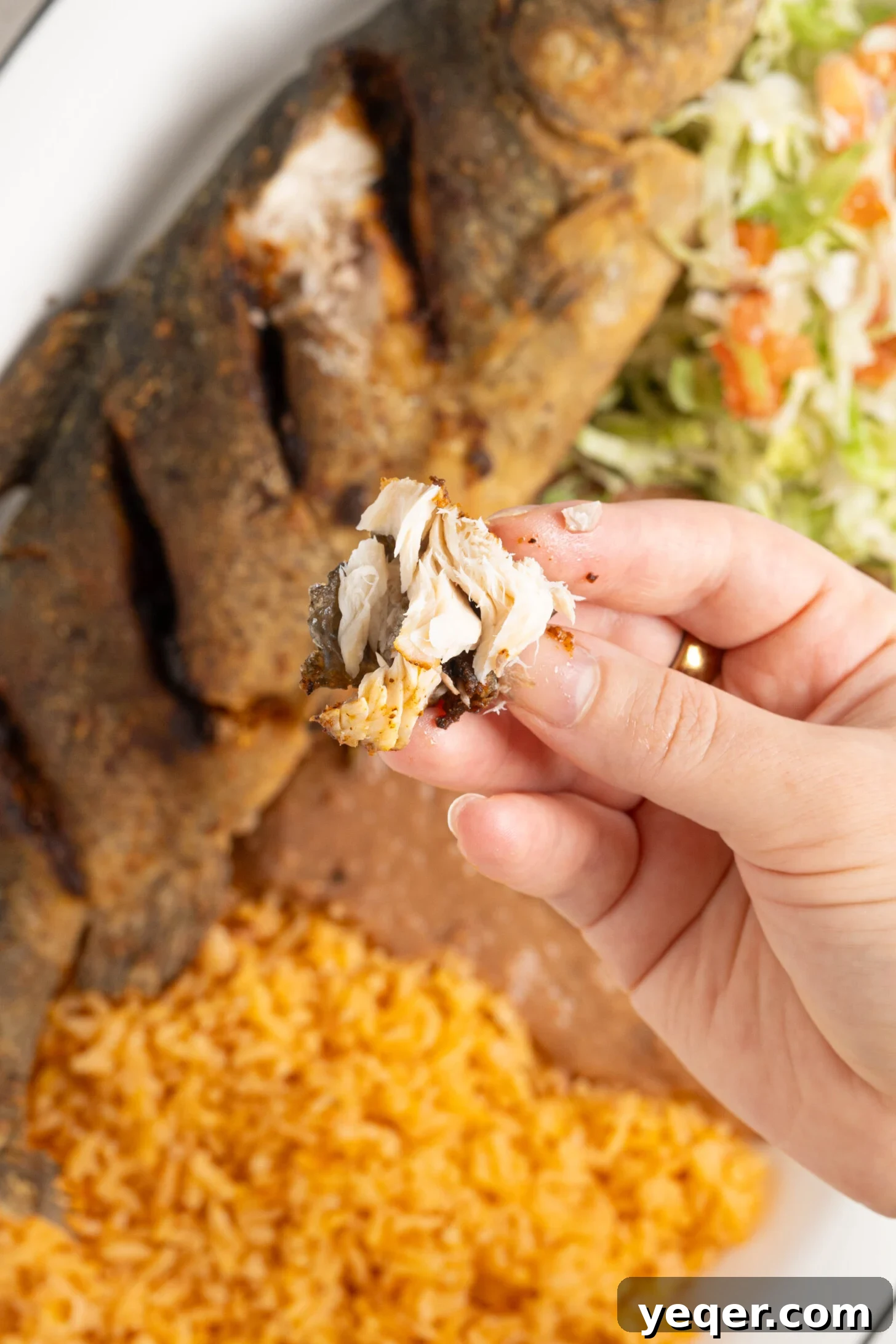 Crispy Whole Fried Mojarra 10 A hand gently holds up a flaky, golden piece of perfectly fried fish, showcasing its crispy texture and tender interior.