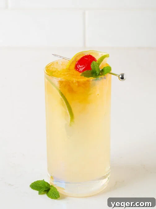 A Mai Tai cocktail garnished with mint and a lime wedge, sitting on a white counter.