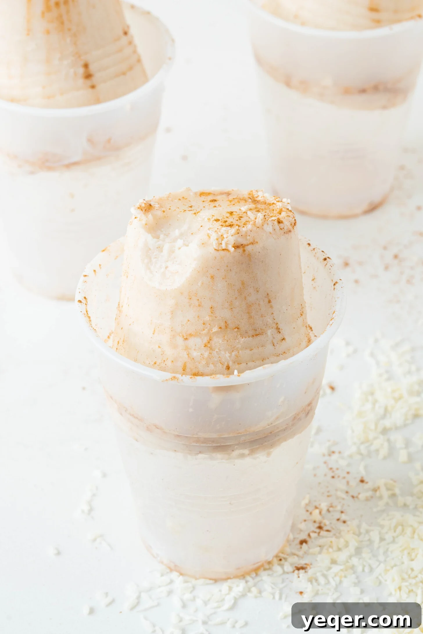 Puerto Rican Limber Coconut Pops 10 A vibrant Limber de Coco in a plastic cup, beautifully garnished with shredded coconut and a sprinkle of cinnamon, against a bright background.