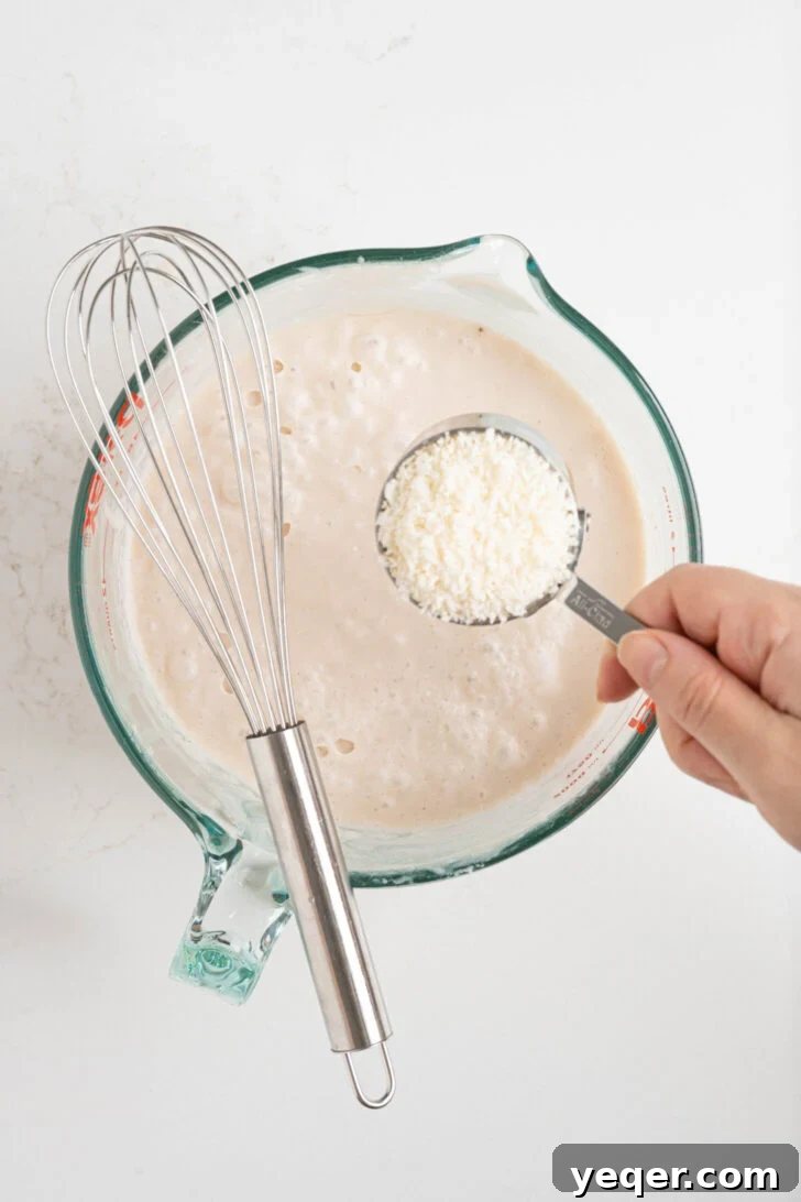 Puerto Rican Limber Coconut Pops 5 Sweet shredded coconut being carefully poured into a large pitcher filled with the creamy, blended coconut milk mixture.