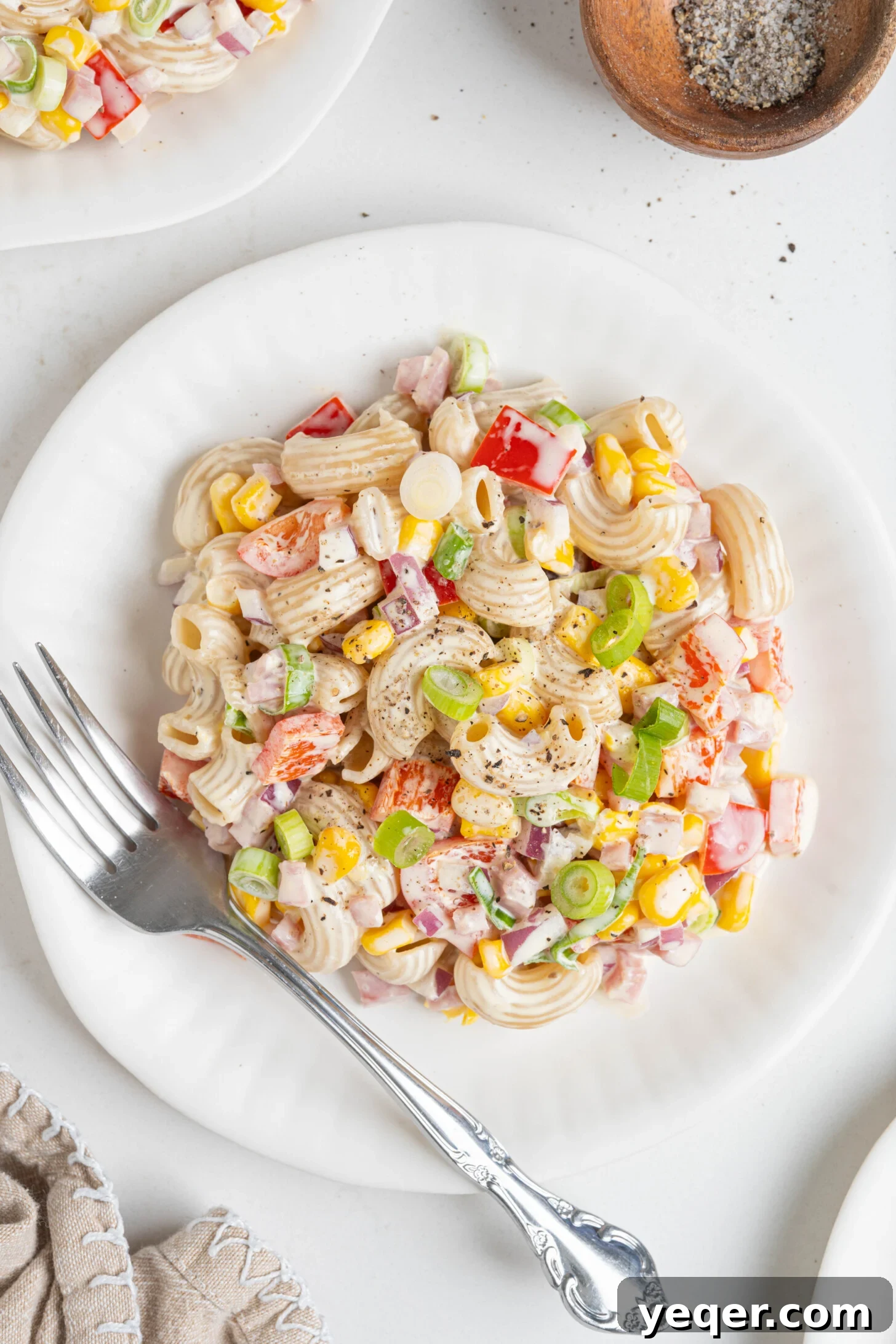 Signature Puerto Rican Macaroni Salad 2 A vibrant plate of Puerto Rican macaroni salad (Ensalada de Coditos) with ham and colorful vegetables, garnished with fresh herbs.