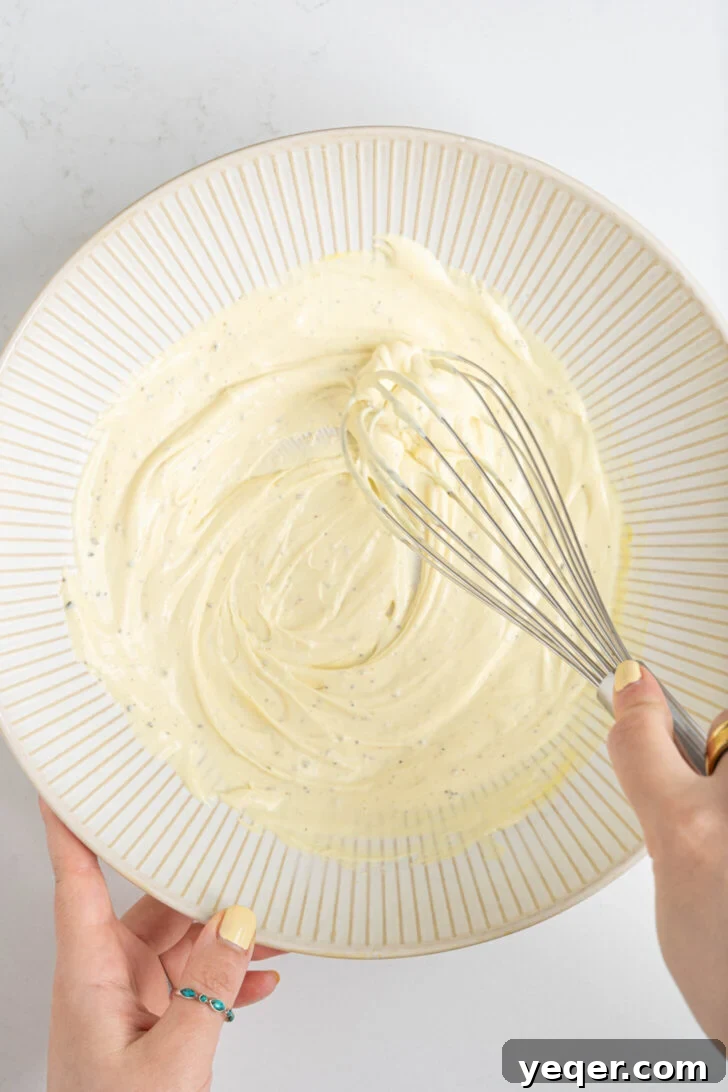 Signature Puerto Rican Macaroni Salad 5 Macaroni salad dressing being whisked in a large bowl, combining mayonnaise, mustard, and vinegar for a creamy texture.
