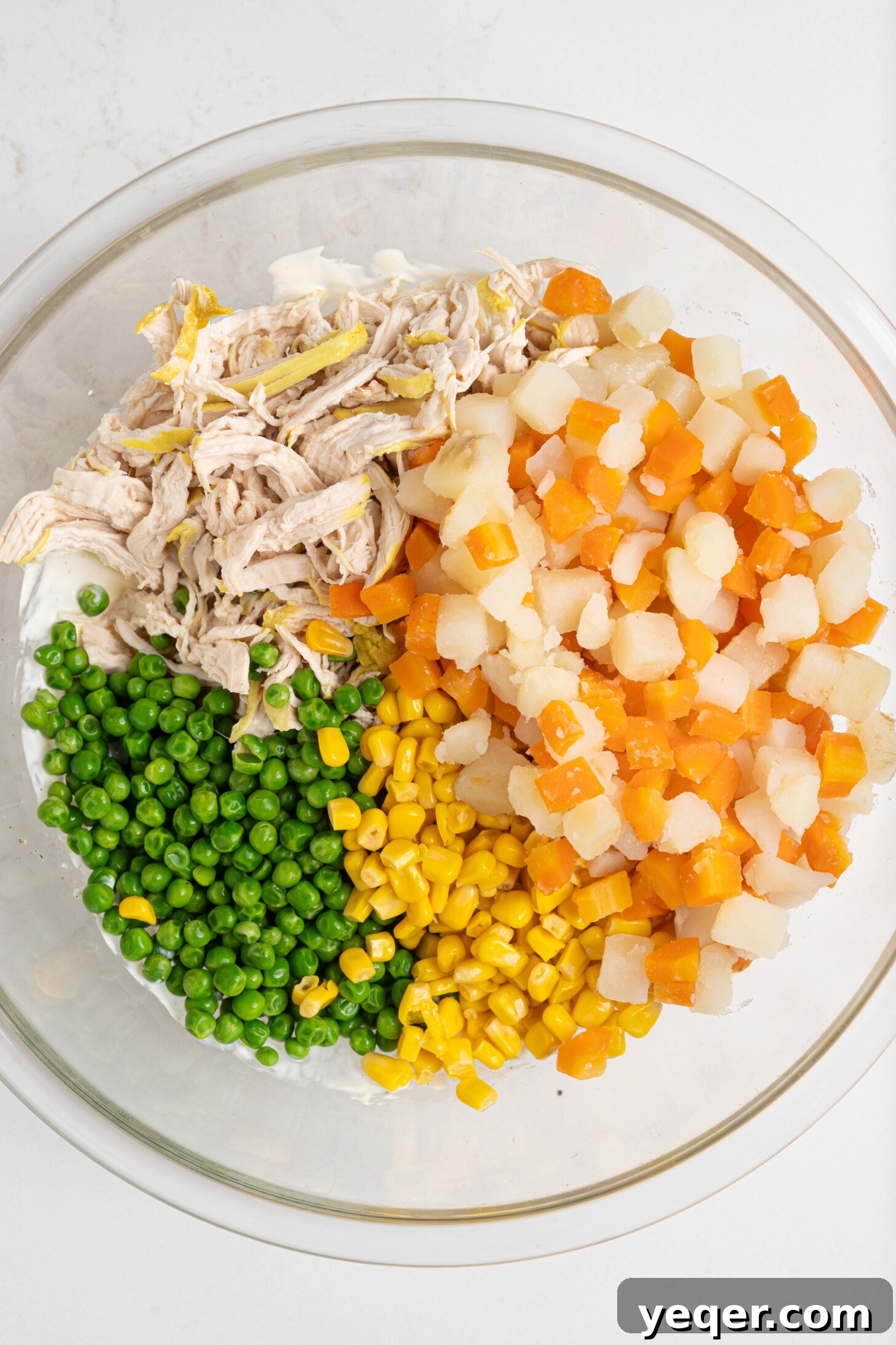 Fiesta Chicken Salad 9 A close-up of a bowl filled with shredded chicken, peas, corn, and other colorful vegetables, lightly coated in dressing.