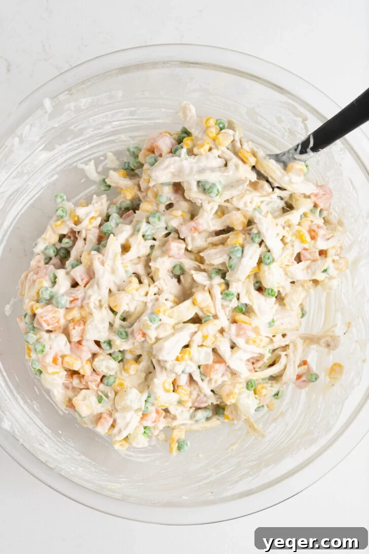 Fiesta Chicken Salad 7 A bowl of ensalada de pollo, with shredded chicken, potatoes, carrots, corn, and peas, all coated in the creamy dressing.