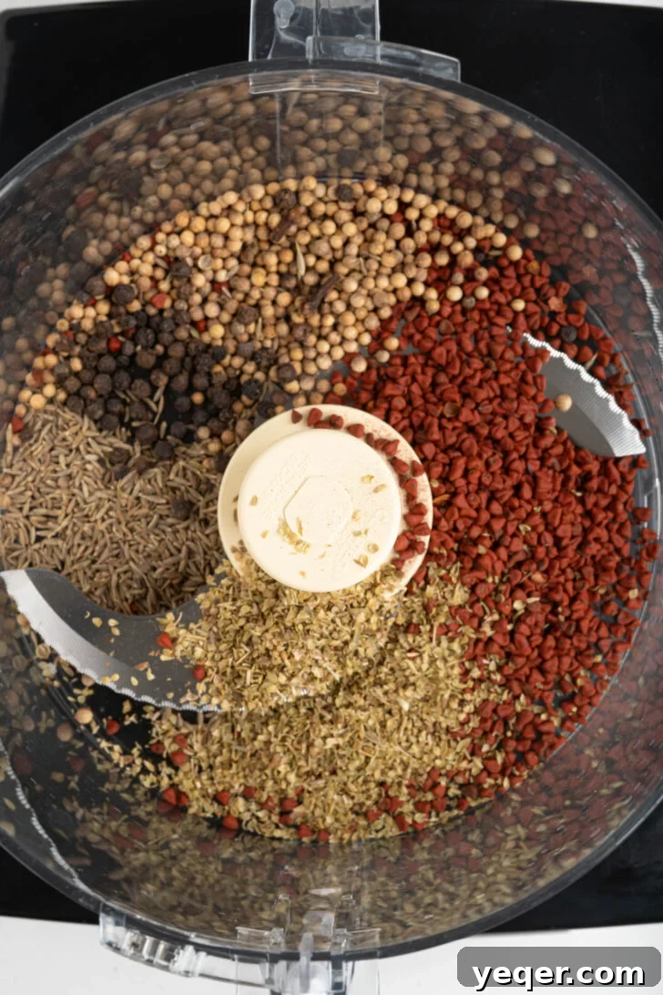 Homemade Achiote Paste in Minutes 5 A food processor bowl filled with whole annatto seeds, coriander seeds, oregano, cumin seeds, peppercorns, and cloves, ready for grinding.