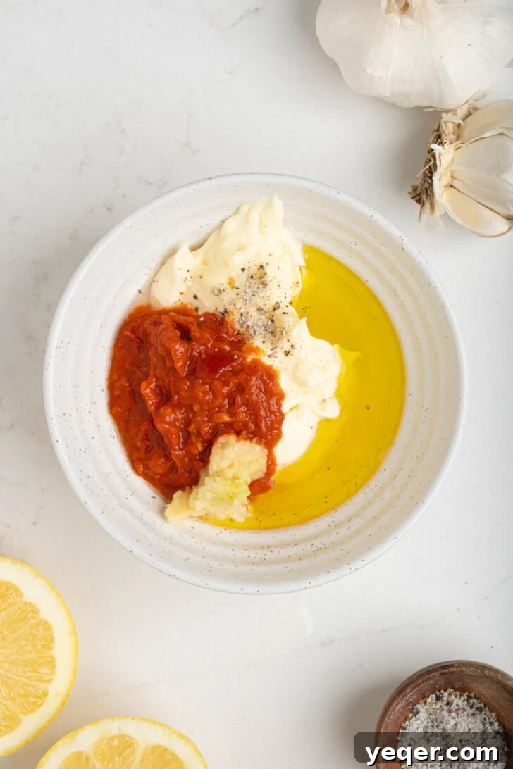 Quick Burst Harissa Garlic Aioli 5 A bowl containing mayonnaise, harissa paste, grated garlic, and lemon juice, ready to be combined.