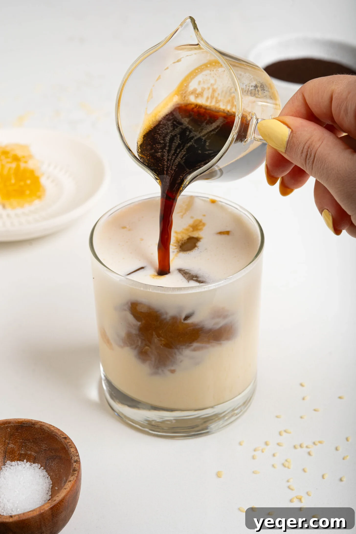 Salty Sweet Honeycomb Tahini Latte 8 Espresso being poured gracefully over frothy tahini honey milk in a glass, creating a beautiful layered effect.