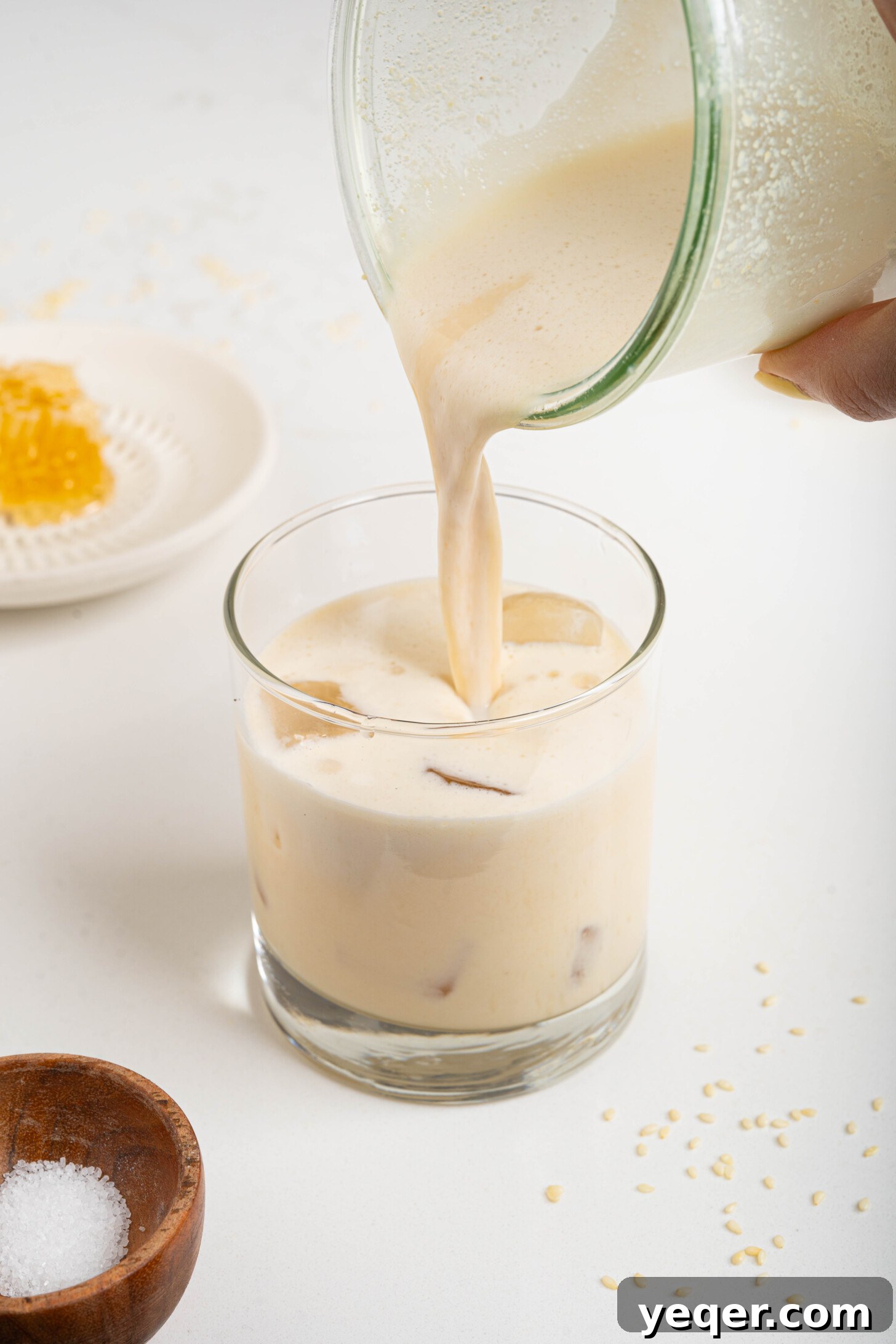 Salty Sweet Honeycomb Tahini Latte 7 Stream of frothy tahini honey milk pouring into a clear glass, creating a swirling pattern.