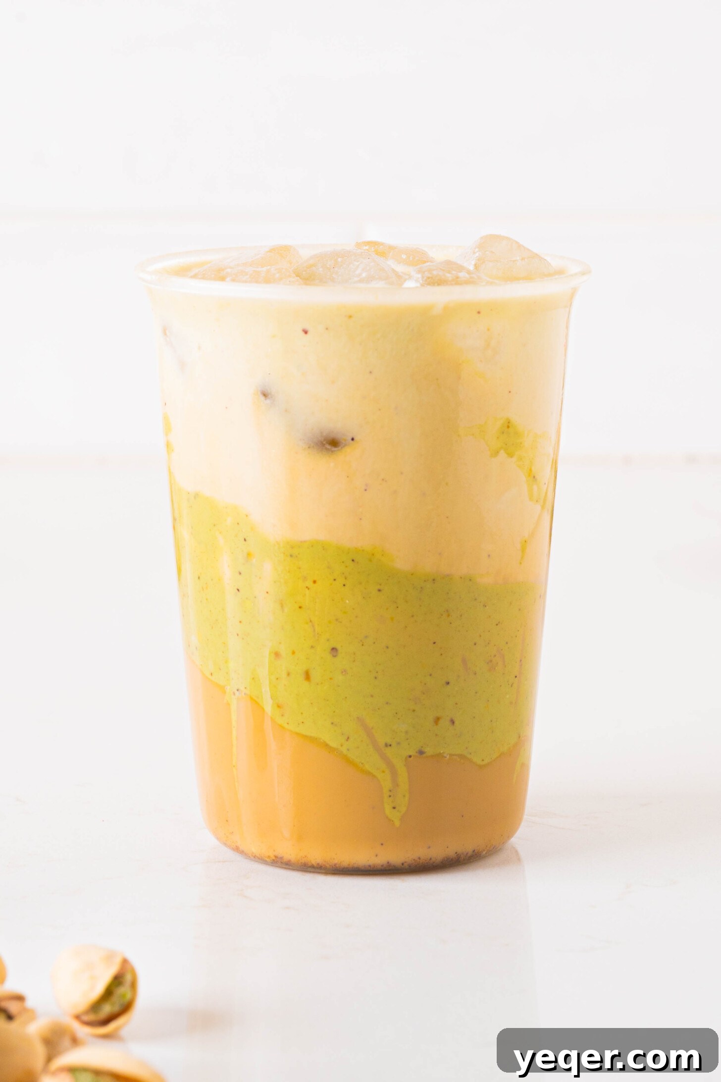 Signature Pistachio Dream Latte 3 A glass filled with a pistachio latte, topped with cold foam and a sprinkle of chopped pistachios.
