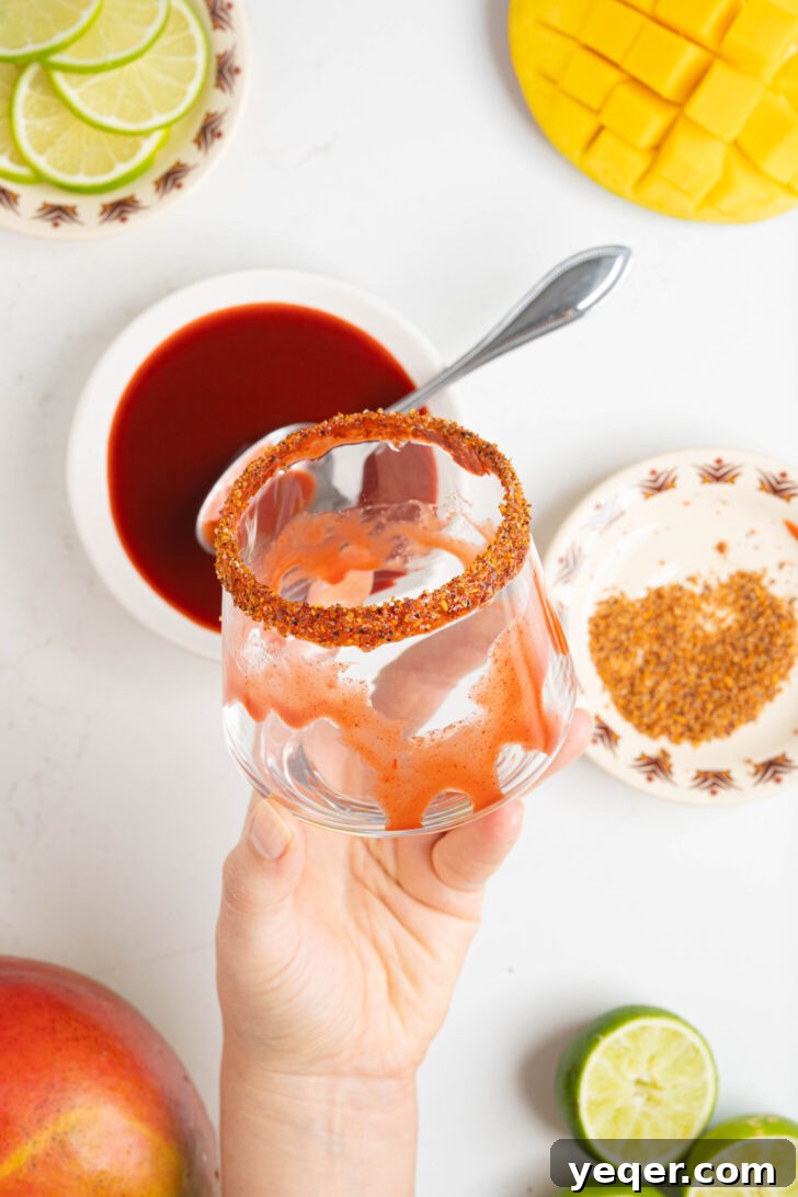 Golden Mango Margarita Bliss for All 4 A clear glass with a vibrant red chamoy smear on the inside and a spicy Tajin rim, ready for a mango margarita.