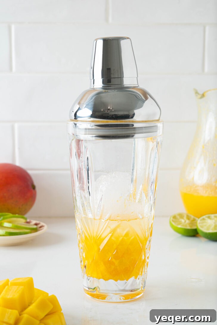 Golden Mango Margarita Bliss for All 6 A cocktail shaker filled with mango puree, lime juice, tequila, orange liqueur, and ice, ready to be shaken.
