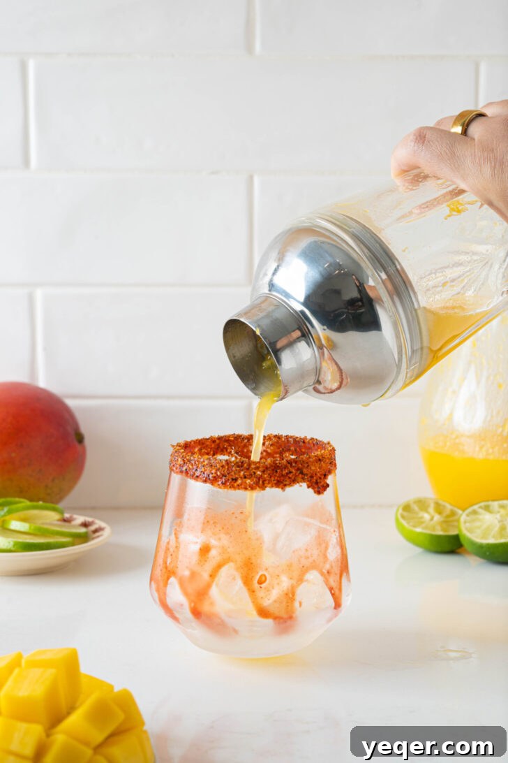 Golden Mango Margarita Bliss for All 7 A fresh mango margarita mixture being strained from a cocktail shaker into a prepared glass filled with ice, ensuring a smooth, pulp-free drink.