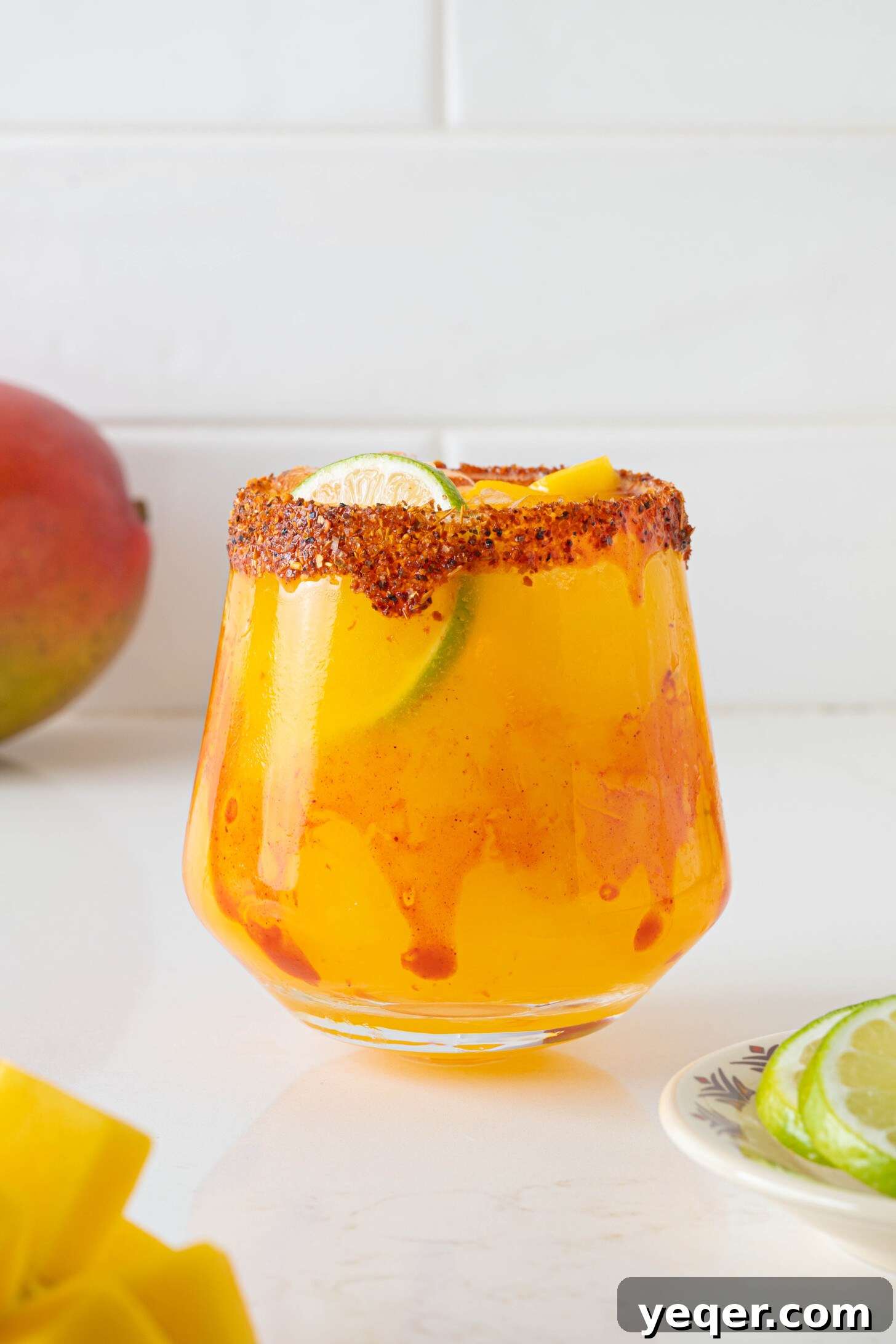 Golden Mango Margarita Bliss for All 8 A close-up shot of a single fresh mango margarita, highlighting its golden hue, the textured Tajin rim, and a vibrant lime wheel garnish, making it irresistibly appealing.