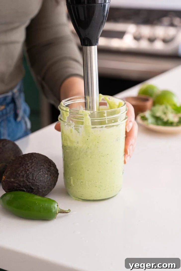 Velvety Greek Yogurt Avocado Dip 6 An immersion blender actively blending the ingredients in a jar to create a smooth avocado dip.