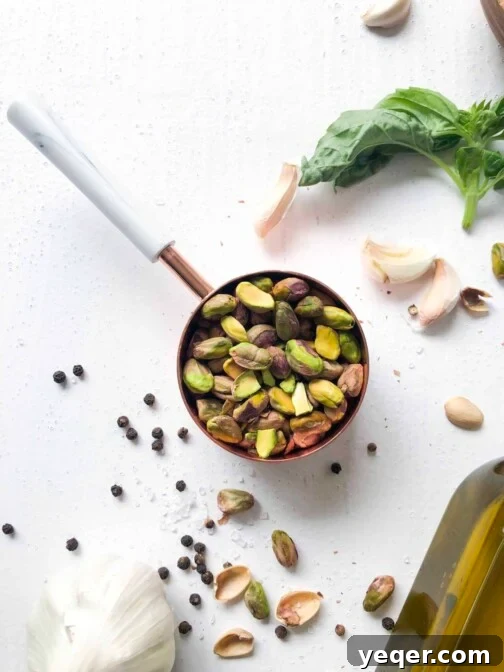 A measuring cup with pistachios next to olive oil, basil, salt and garlic, ready for making pesto.