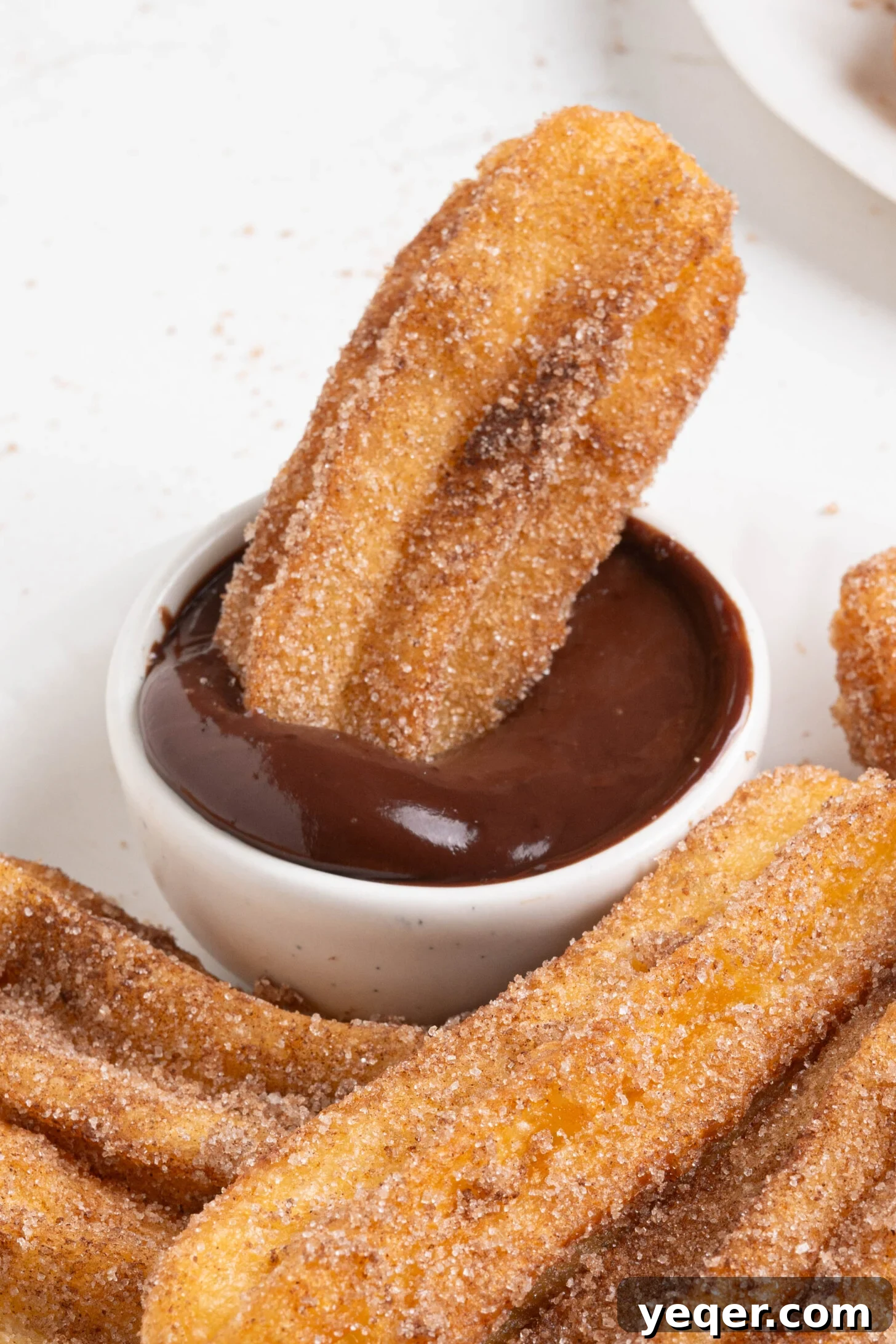 Homemade Golden Churros with Decadent Chocolate Sauce 11 A homemade churro perfectly dipped into a bowl of rich chocolate sauce, ready to be enjoyed.