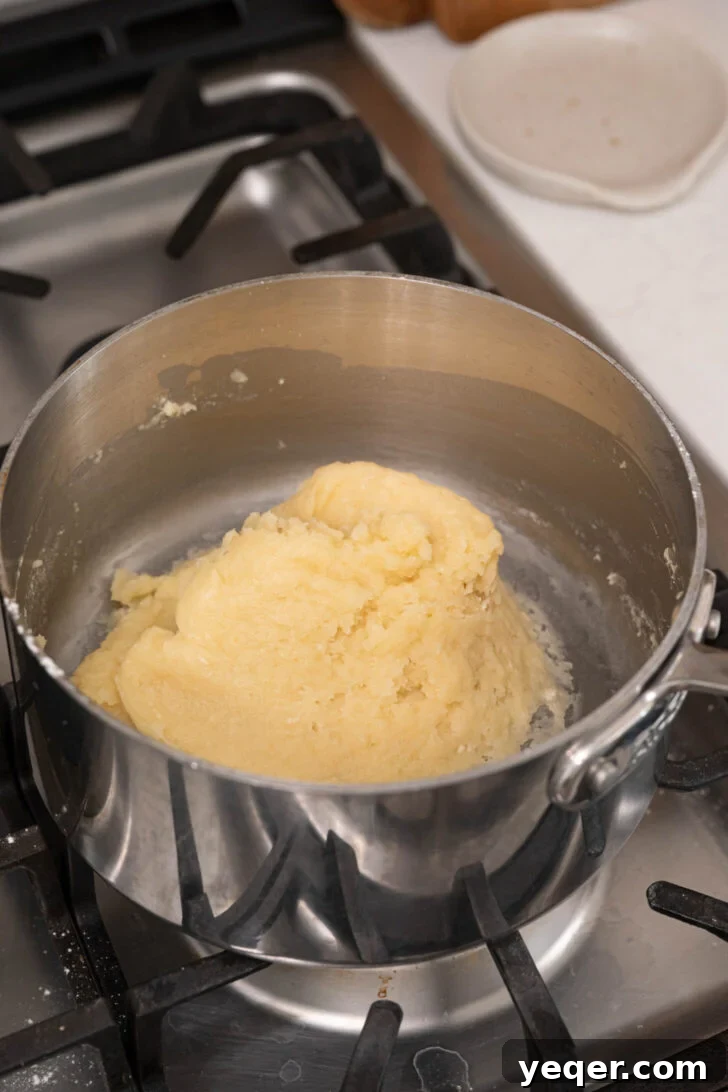 Homemade Golden Churros with Decadent Chocolate Sauce 6 The choux pastry dough forming in a pot after flour is added, being stirred with a spatula.