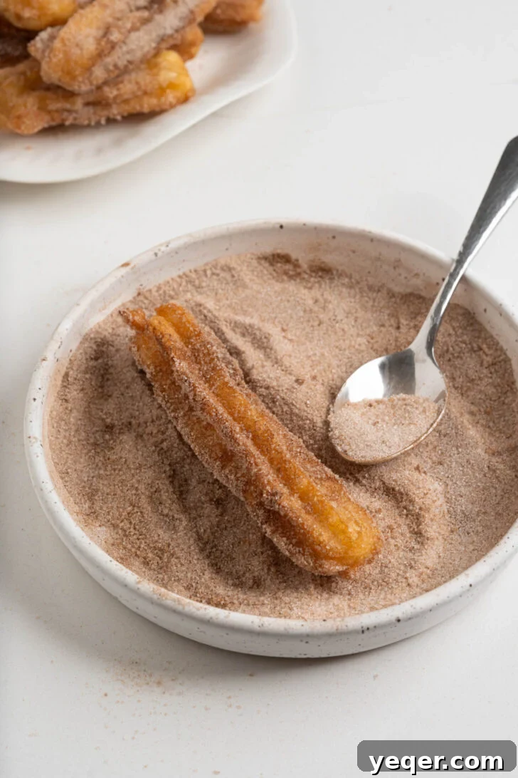 Homemade Golden Churros with Decadent Chocolate Sauce 9 A fried churro being rolled in a bowl of cinnamon sugar for coating.