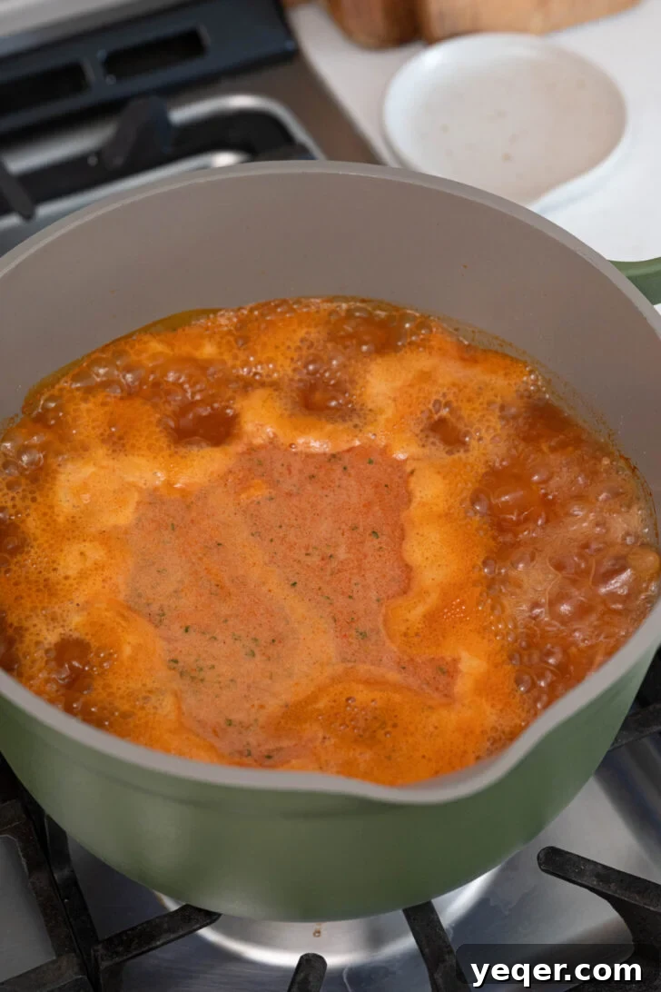 Vibrant Tomato Vermicelli Soup 7 A pot of Sopa de Fideo simmering on the stove, with potatoes, tomato sauce, broth, and cilantro sprigs visible in the rich, red liquid.
