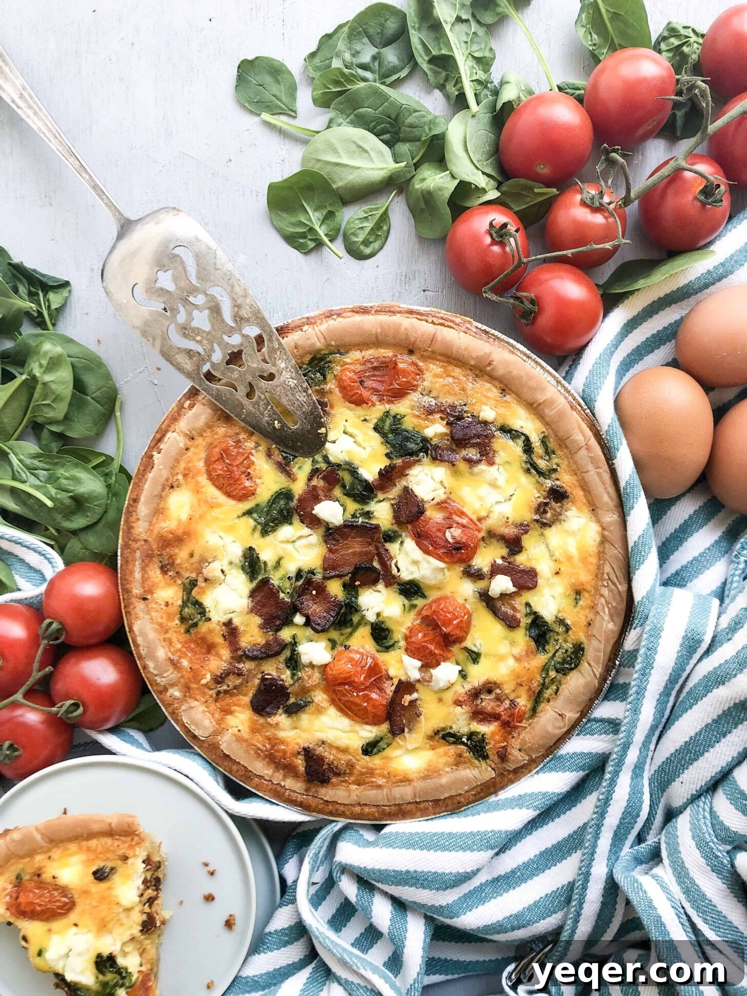 Mother's Day Brunch Dream Quiche 2 A beautifully baked Mother's Day Quiche, rich with bacon, spinach, tomatoes, and goat cheese, presented alongside a subtly striped kitchen towel, ready to be served for a festive brunch.