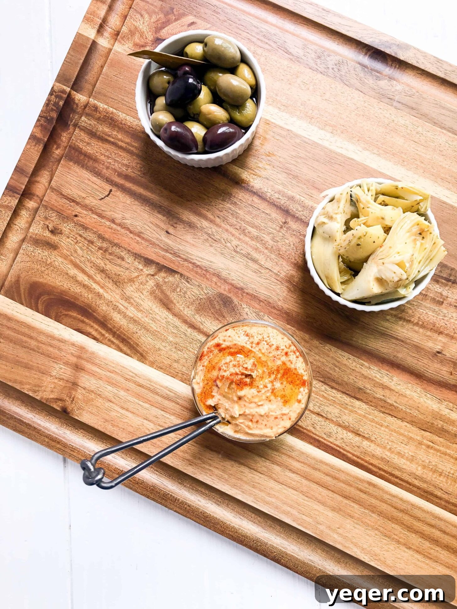 Botanical Bites Board 3 A rustic cutting board adorned with vibrant green olives, creamy hummus, and tender artichoke hearts, ready to be incorporated into a larger charcuterie spread.
