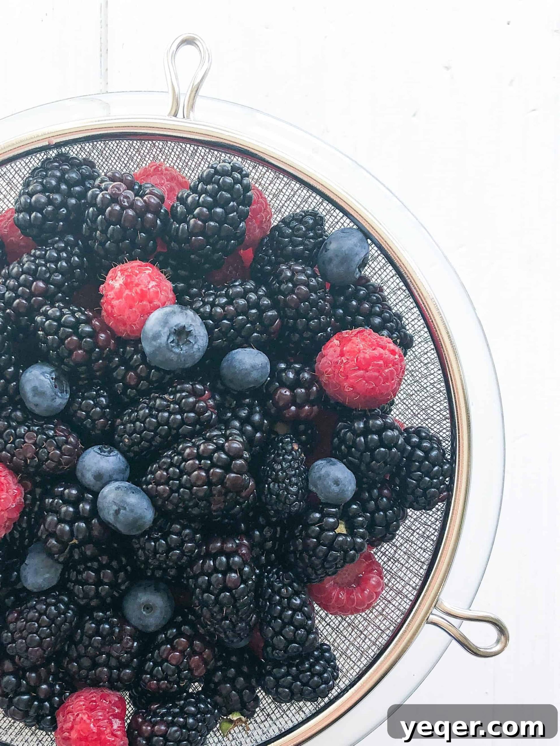 Heavenly Gluten Free Berry Crumble 3 Freshly rinsed and vibrant mixed berries, including raspberries, blueberries, and marionberries, gleaming in a colander, ready for the gluten-free crisp preparation.