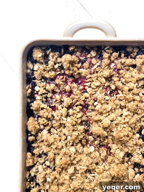 A perfectly baked gluten-free berry crisp, with a golden-brown, bubbly top and juicy berry filling, presented in a white baking dish.