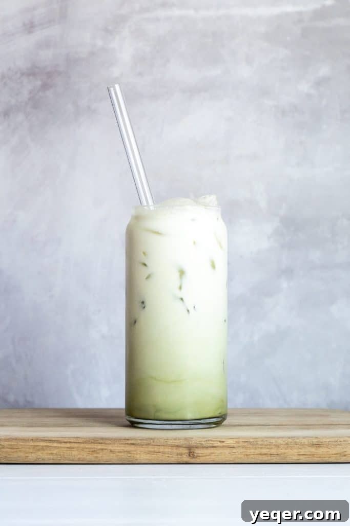 Effortless 4-Ingredient Matcha Lattes, Whisk-Free 2 A vibrant green iced matcha latte, topped with frothy milk, in a tall glass.
